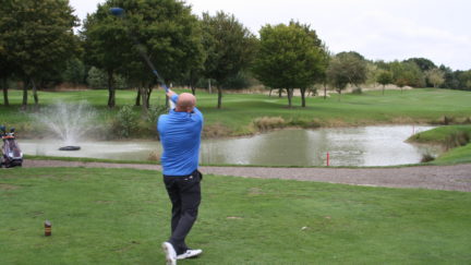 Photo of man swinging golf club next to lake