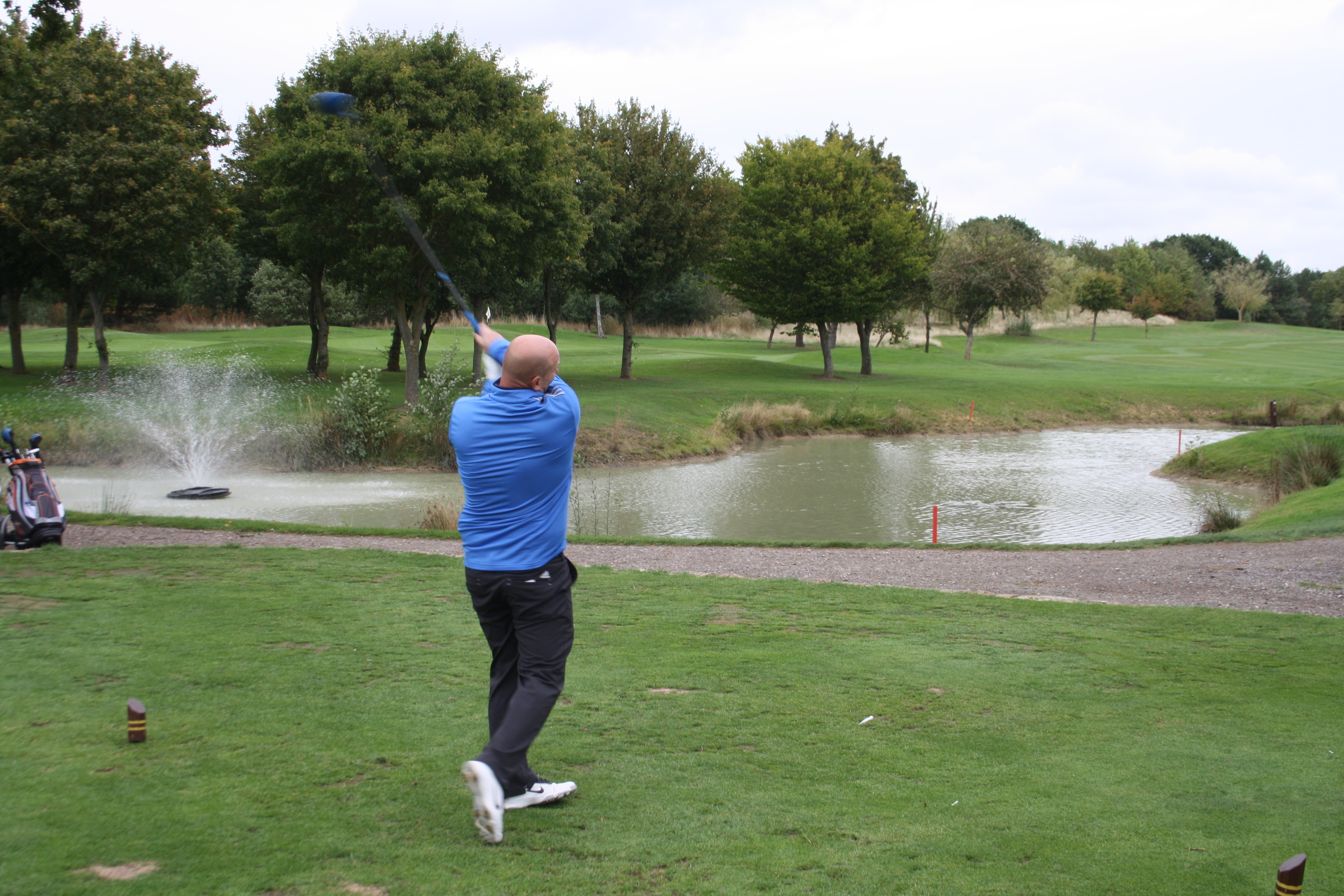 Photo of man swinging golf club next to lake